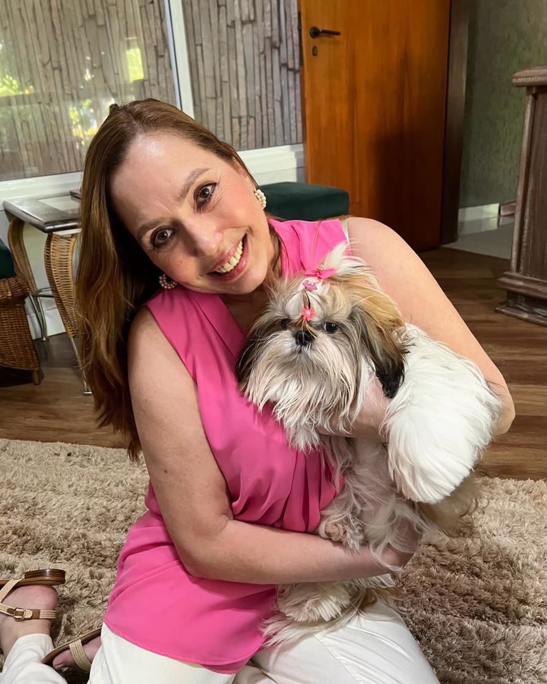 Mirabelle at home on a rug, holding Lula, a grown gold and white Shih Tzu with bows in her topknot