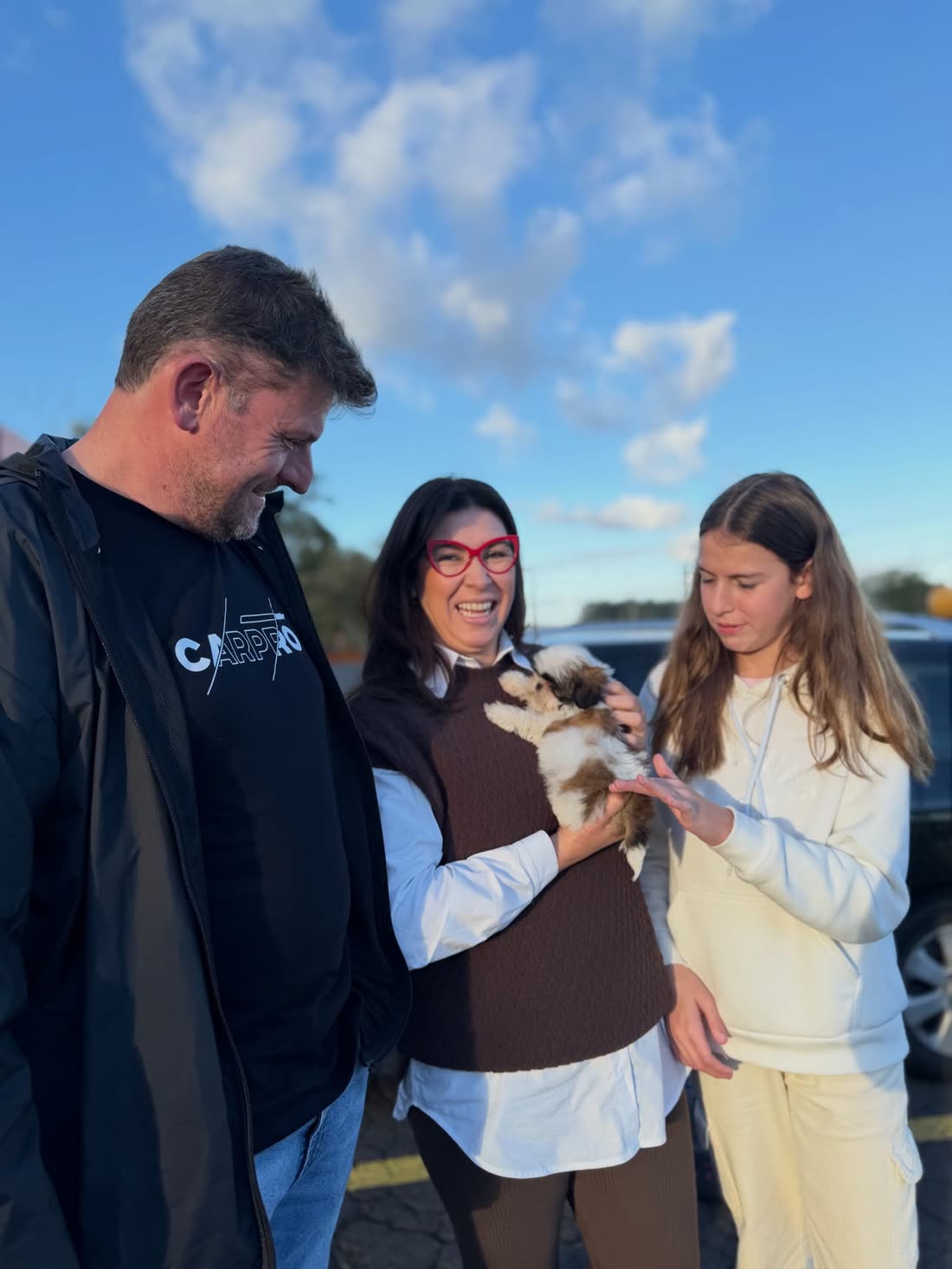 The Harpson family standing beside their car on the day they collected Milo, a brown and white Shih Tzu puppy