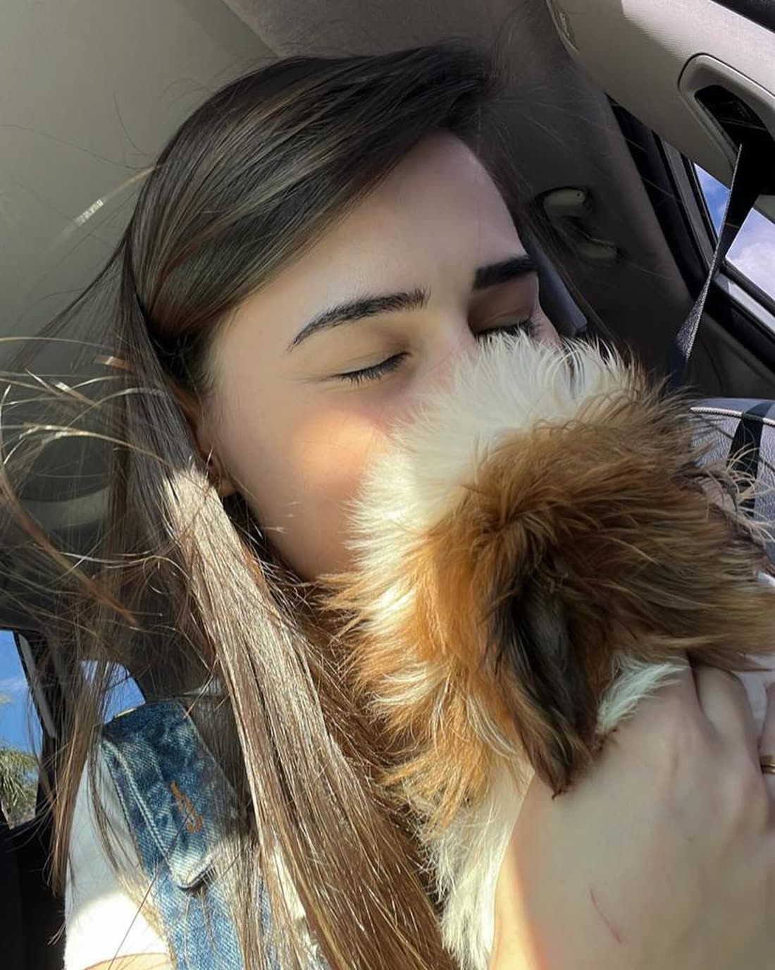 Sardie in her car with her eyes closed, holding Queen, a gold and white Shih Tzu puppy, to her face