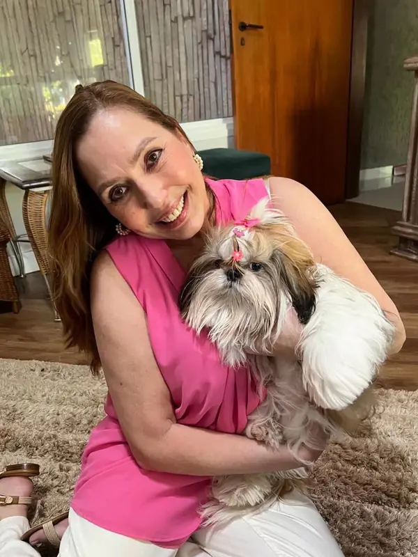 Mirabelle at home on a rug, holding Lula, a grown gold and white Shih Tzu with bows in her top knot